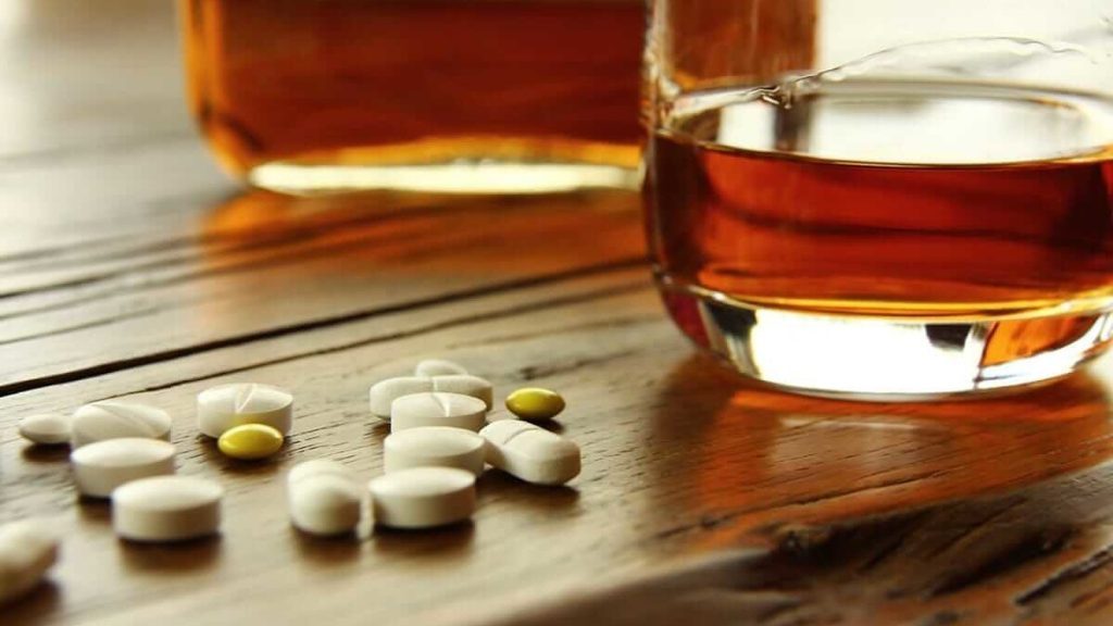 Glass of alcohol and pills on a table, symbolizing alcohol and drugs