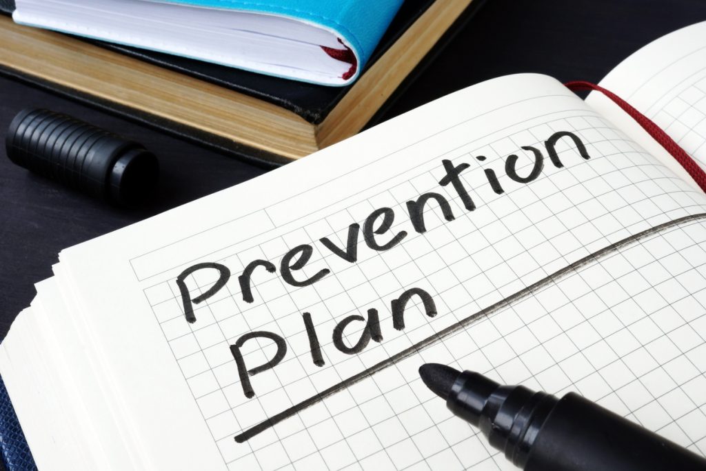 Notebook with "Prevention Plan" written on grid paper, marker nearby