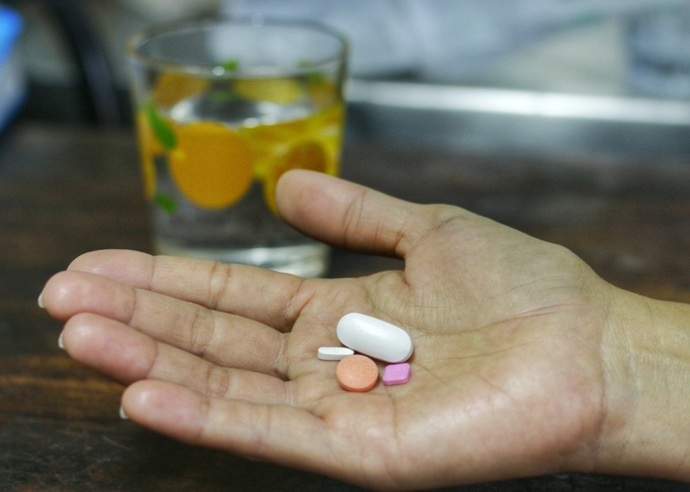 Hand holding pills with a glass behind, effects of alcohol on the heart