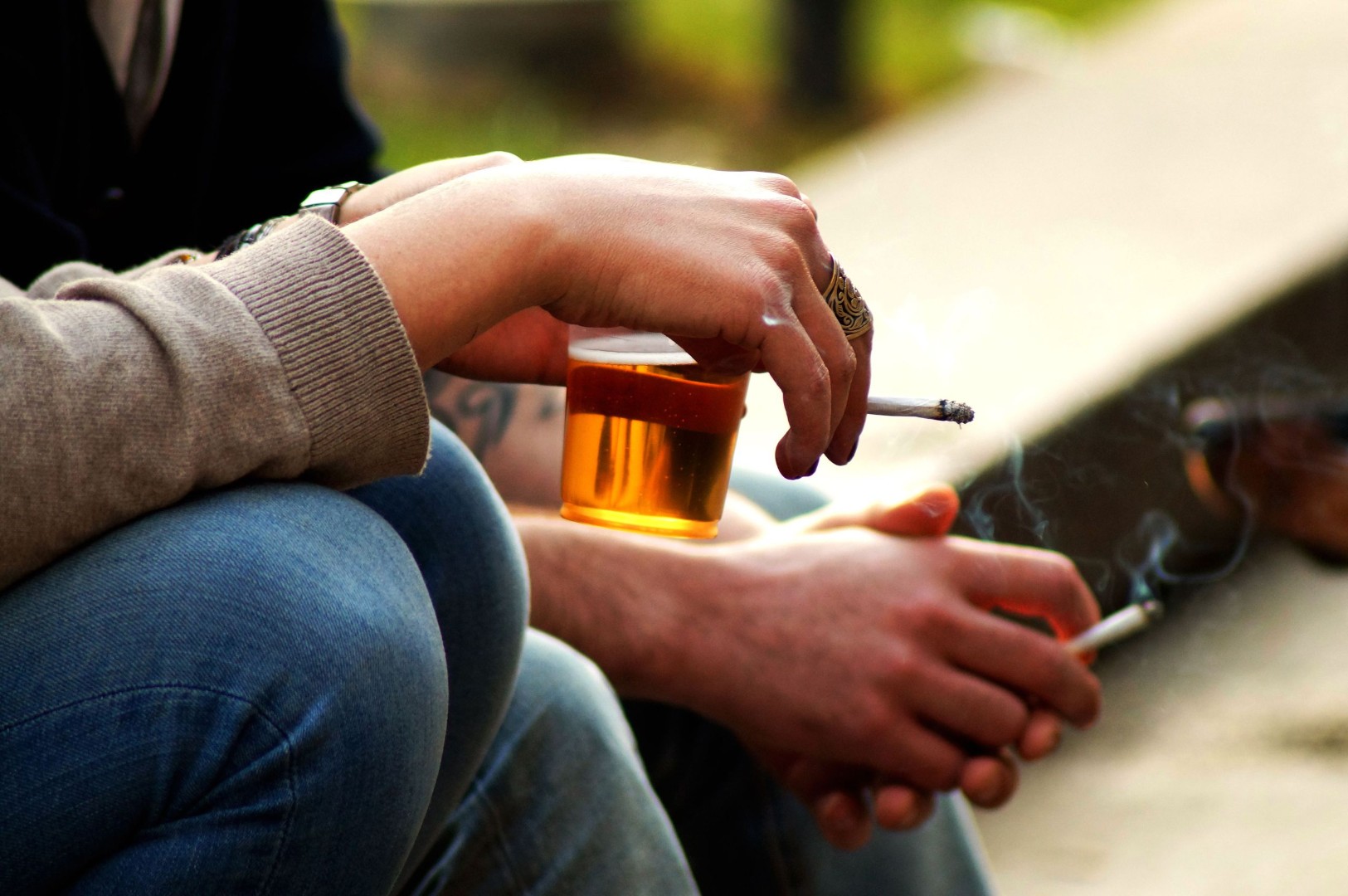 Two people holding drinks and cigarettes, exploring links to pancreatitis and alcohol.