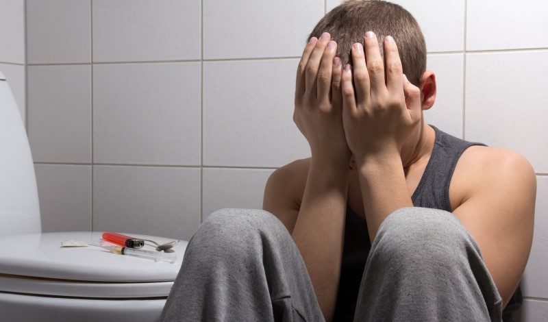 Overcoming Heroin Addiction: Start Your Rehab Journey Today Man struggling with heroin addiction sitting on bathroom floor